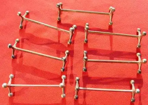 () Sieben uralte, originale Messerbänkchen. Länge ca. 10 cm. Höhe ca. 3,5 cm. Jedes Teil ist mit Herstellerzeichen versehen : Berndorf A. S. Soweit ich den Zustand beurteilen kann, sind die Teile in Ordnung und ungeputzt. Metall Silber ?...