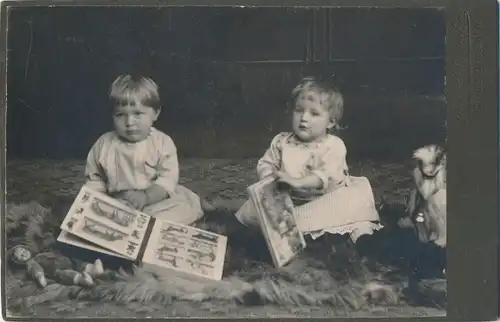Foto Zwei Kinder mit Spielzeugen auf einem Fell sitzend, Bilderbücher, Puppe