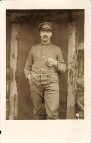 Foto Ak Soldat in Uniform mit Zigarre in der Hand vor einer Holzhütte, I. WK