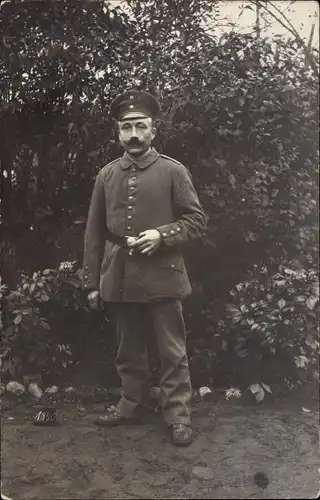 Foto Ak Deutscher Soldat in Uniform, Standportrait in einem Garten, Zigarre rauchend