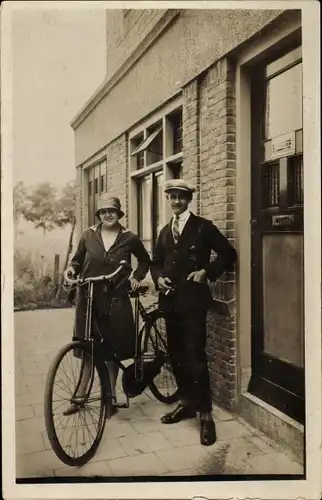 Foto Ak Paar vor einem Haus, Frau mit Fahrrad, Hut, Mantel, Mann Zigarette rauchend