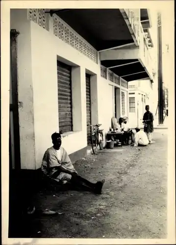 Foto Ak Kindia Guinea, Hommes assis sur le Bord de la Rue