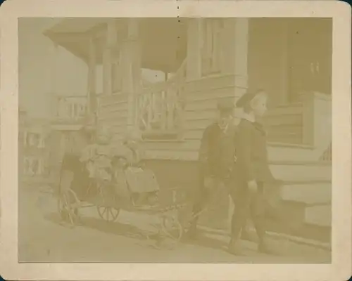 Kabinett Foto Jungen ziehen Mädchen auf einem Bollerwagen, Portrait vor Hausveranda