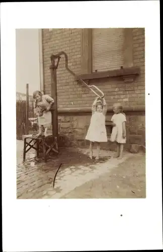 Foto Drei Mädchen spielen an der Wasserpumpe