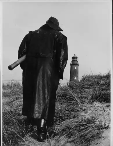 Foto Mann im Regenmantel mit Fernrohr auf dem Weg zum Leuchtturm, Fotog. Hilde Zenker, Berlin