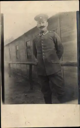 Foto Ak Deutscher Soldat in Uniform vor einer Baracke, Portrait