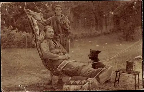 Foto Ak Frau mit Zigarette im Bademantel, Mann in einer Hängematte, Hund