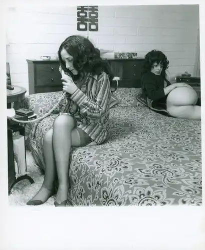 Akt Fotografie, Frau nacktes Gesäß auf einem Bett liegend, zweite Frau telefonierend, sitzt daneben