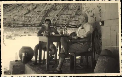 Foto Guinea, Männer am Tisch, Alkohol, Flaschen, Hütte, Strohdach