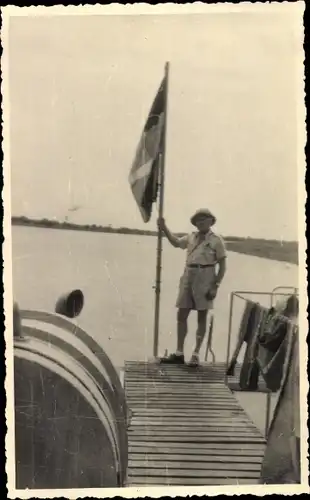 Foto Ak Guinea, Mann mit Flagge, Kolonist auf einem Bootssteg