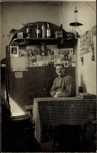 Foto Ak Deutscher Soldat in Uniform an einem Tisch, Ansichtskarten an der Wand, I WK