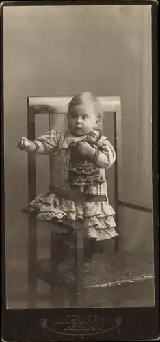CdV Kinderportrait, Kleinkind mit Puppe auf einem Stuhl stehend, Hilde, 1910