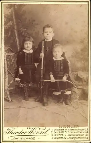 Kabinettfoto Kinderportrait, Drei Kinder mit Spielzeugen, Gewehr, Peitsche