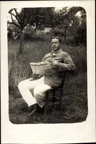 Foto Ak Deutscher Soldat in Uniform, Sitzportrait auf einem Stuhl, Zeitung, Oynes 1915