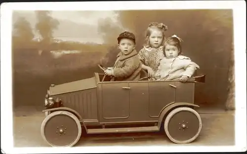 Foto Ak Kinder in Spielzeugauto, Junge und zwei Mädchen