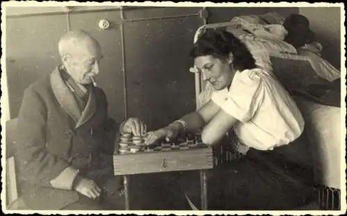 Foto Ak Alter Mann im Mantel mit Zigarre und Frau beim Damespiel, Bett
