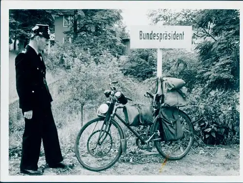 Foto Polizist in Uniform, bepacktes Fahrrad an ein Schild gelehnt, Aufschrift Bundespräsident