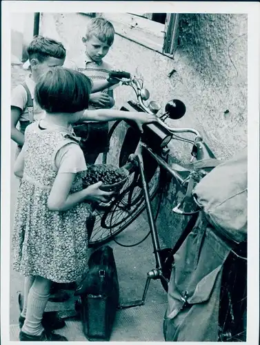 Foto Kinder betrachten an Hauswand gelehntes Fahrrad, Koffer, Korb mit Kirschen