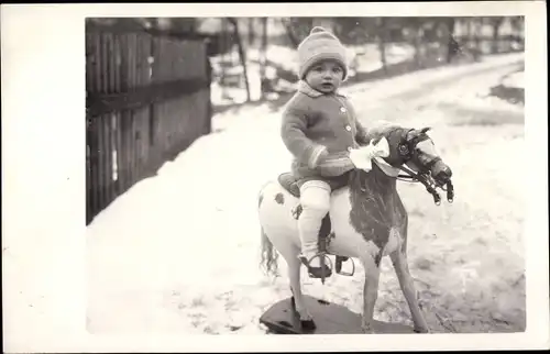 Foto Ak Kind auf einem Spielzeug-Pferd sitzend, Winterszene