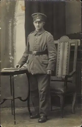 Foto Ak Deutscher Soldat in Uniform, Standportrait, Stuhl, Tisch