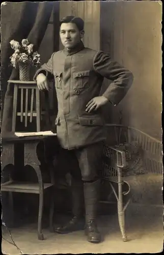 Foto Ak Deutscher Soldat in Uniform, Standportrait, Tisch, Blumen