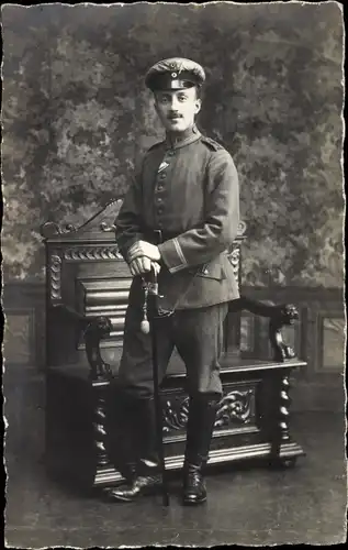 Foto Ak Deutscher Soldat im Atelier stehend, Schirmmütze, Säbel