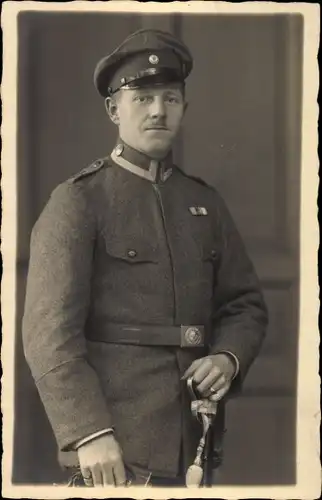 Foto Ak Deutscher Soldat in einem Atelier stehend, Schirmmütze, Säbel