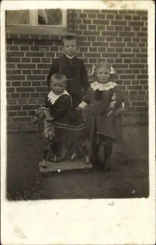 Foto Ak Kinderportrait, drei Kinder, Spielzeugpferd, Mädchen mit Puppe
