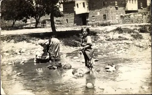 Foto Ak Frau wäscht Kleidung, Mädchen im Wasser, Im Hintergrund Häuser