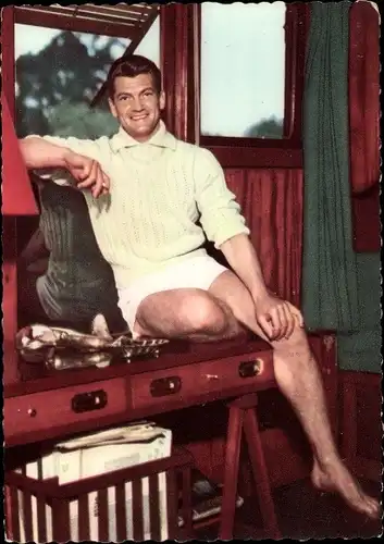 Ak Schauspieler Jean Marais, Portrait in kurzen Hosen auf einem Tisch sitzend, Ufa Film