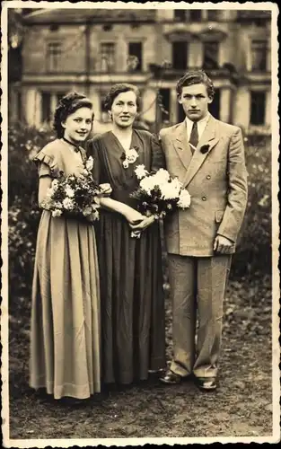 Foto Ak Bützow in Mecklenburg, Mann und zwei junge Frauen, Standportrait, Anzug, Kleider, Blumen