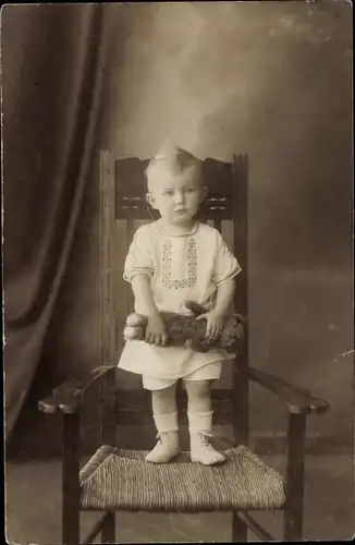 Foto Ak Kleinkind mit Teddy steht auf einem Stuhl, Portrait