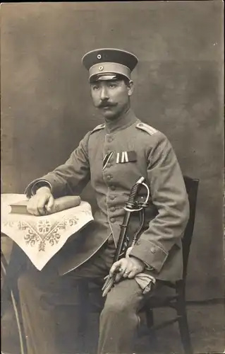 Foto Ak Deutscher Soldat in Uniform, Portrait am Tisch, Kaiserzeit, Säbel