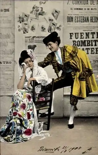 Ak Paar in spanischen Tracht envor einer Wand mit Zeitungsausschnitten