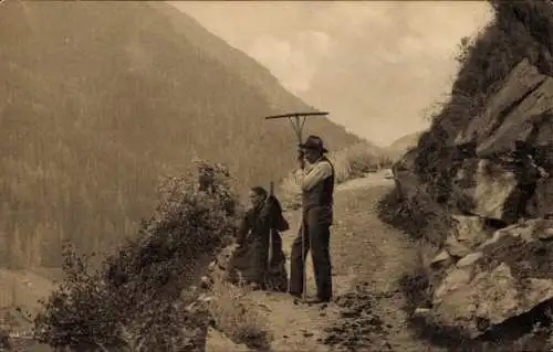 Ak Kanton Wallis, Ehepaar in schweizerischer Tracht, Harke, Berge