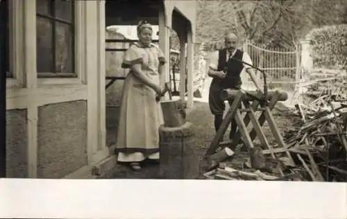 Foto Ak Ehepaar, Wohnhaus, Mann sägt Holz, Holzstück