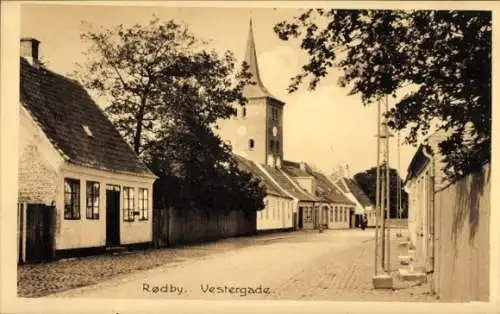 Ak Rødby Dänemark, Rødby. Vestergade. Kleinstadt mit Kirche, Häusern und Bäumen.