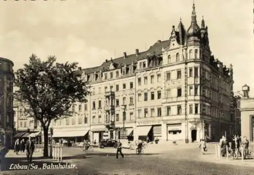 Ak Löbau in Sachsen, Straßenszene mit Passanten, Bäumen und einem großen Gebäude im Hintergrund