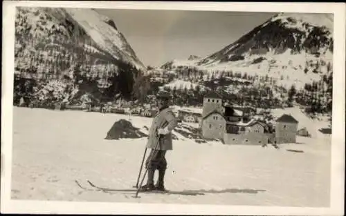 Ak Davos Kanton Graubünden, Mann mit Skiern steht vor verschneitem Hotel mit Bergen im Hinterg...