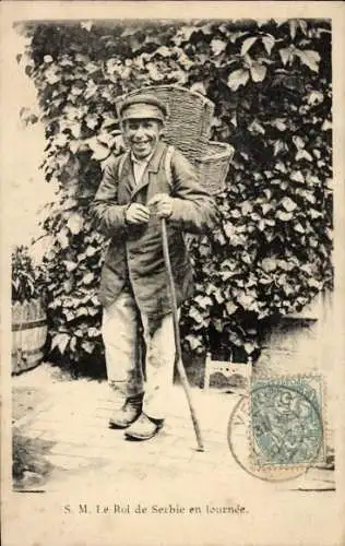 Ak Le Roi de Serbie en tournee, grinsender Mann mit Rückentrage