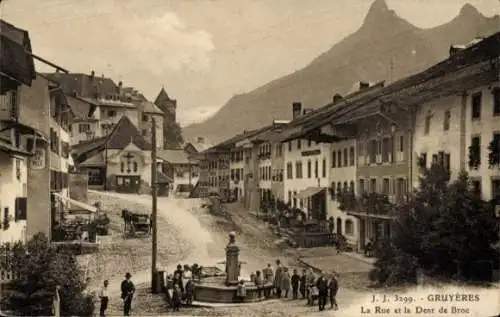 Ak Gruyères Kanton Freiburg Schweiz, Historische Straße, Brunnen, Bergsicht, Häuser, Menschen