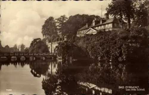 Ak Bad Pyrmont in Niedersachsen, Brücke, Wasserreflexion, Schloss, Bäume, Wolken, historische ...