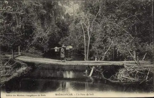 Ak Madagaskar Madagascar, Ein Holzbrücke, Mann mit Last, dichte Vegetation, ruhiges Wasser