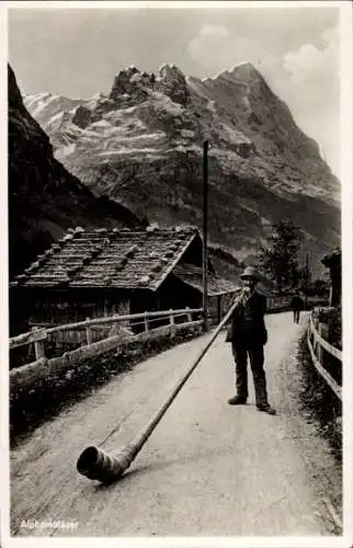 Ak Airolo Kanton Tessin Schweiz, Mann in Tracht mit Alphorn steht vor einem Haus. dahinter sin...