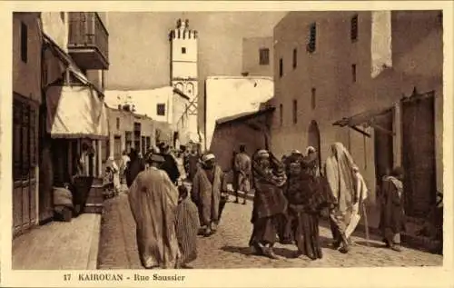 Ak Kairouan Tunesien, Rue Saussier, Menschen auf der Straße, Turm im Hintergrund