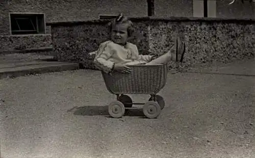 Foto Ak Kinderportrait, kleines Mädchen in einem Puppenwagen aus Korbgeflecht