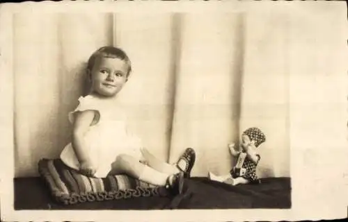 Foto Ak Kinderportrait, Kleinkind auf einem Kissen sitzend, Puppe, 1929