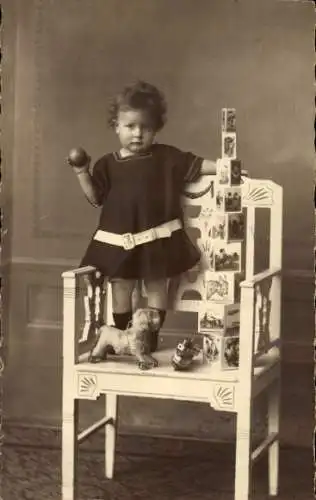 Foto Ak Kinderportrait, Kleinkind mit Spielzeugen auf einem Stuhl, Würfel, Ball, Stoffhund