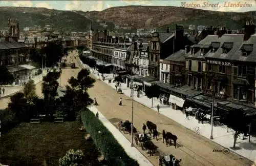 Ak Llandudno Wales, Mostyn Street, Geschäfte, Pferdewagen, Berg im Hintergrund