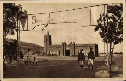 Ak Bamako Mali, Sportgelände, Banner mit "Societé Port Cuvanaise", Gebäude, zwei Personen